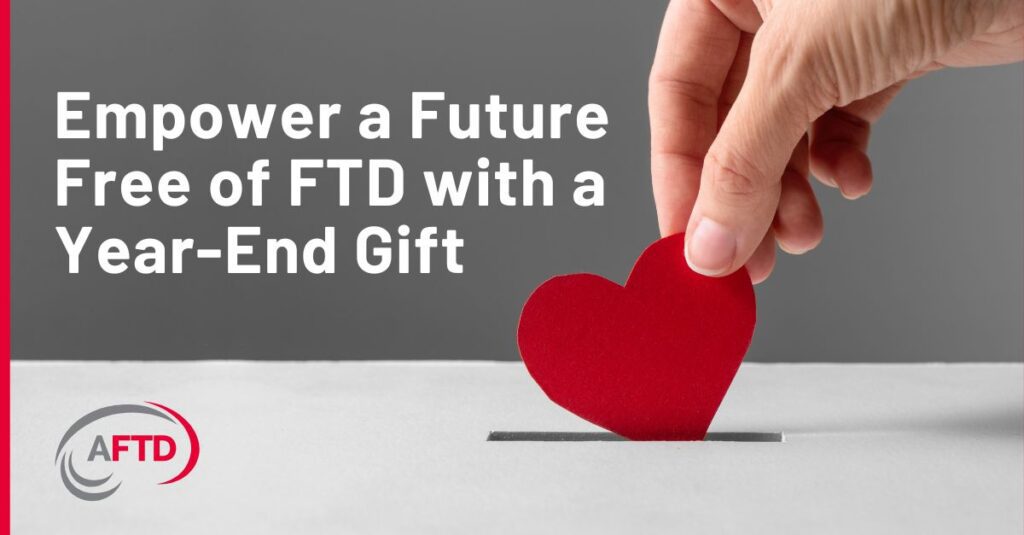 Text: Empower a Future Free of FTD with a Year-End Gift Background: A person inserts a paper heart into a money donation slot